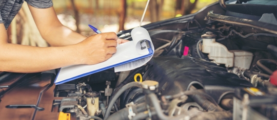 Car mechanic noting repair parts during open car hood engine