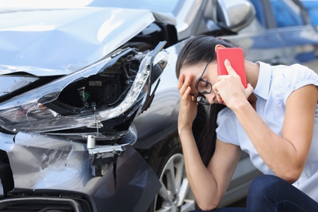 Sad woman talking on cell phone near wrecked car stock photo
