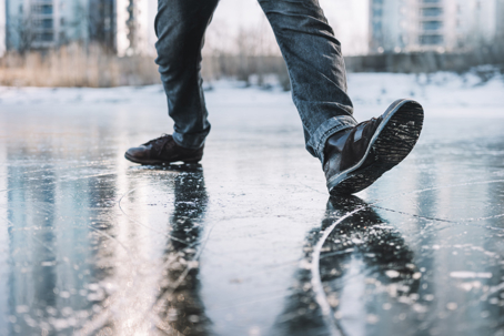 Boots standing on icy ground, illustrating the danger of slipping on a frozen, slippery winter surface. man walks cautiously along an icy street on a winter day for fear of slipping and falling. stock photo
