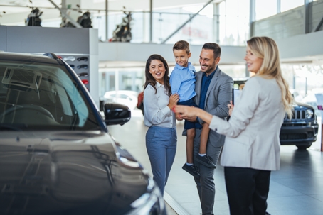 Young happy family enjoying while buying a new car in a showroom.