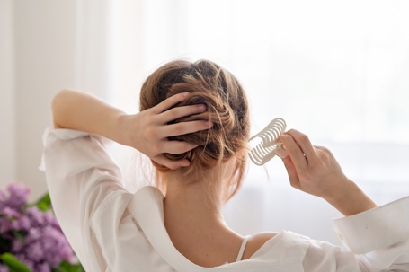 Young woman making messy hair bun, clipping hair with claw clip, back view