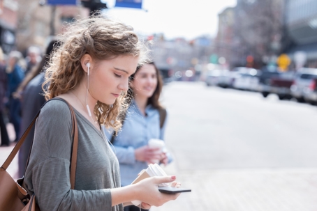 Young woman crosses street distracted by digital media