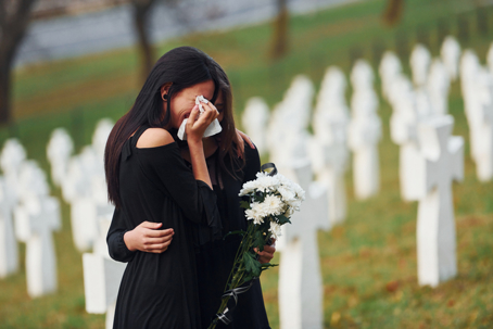 Embracing each other and crying. Two young women in black clothes visiting cemetery with many white crosses. Conception of funeral and death stock photo
