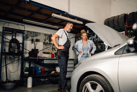 Repairman and customer looking under car hood at mechanic shop