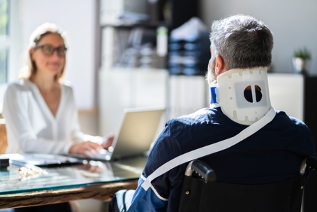 Injured man in a neck brace and wheelchair talking to an attorney
