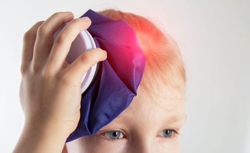 A little girl aged seven holds a cold bag of ice to her head