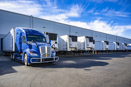 Big rig blue semi truck with refrigerator semi trailer standing in row with another semi trailers in warehouse dock gates loading cargo for the next freight stock photo