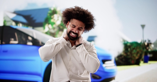 Man experiencing neck pain and stress after car accident near smoking vehicle. Insurance adjuster, auto mechanic, personal injury lawyer.