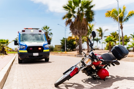 Red motorcycle lying on street after accident with ambulance in background stock photo