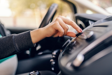 Close up of woman searching radio station while sitting in car. Other hand on steering wheel. stock photo
