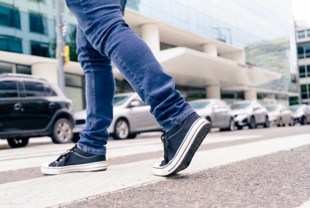 Close-up of the feet of a man in black sneakers crossing a street on the zebra or pedestrian path