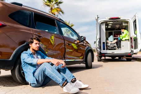 Man sitting on ground after car accident with ambulance in background stock photo