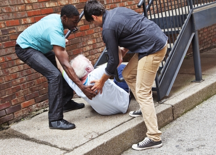 Two young men help an elderly man get back up after falling stock photo