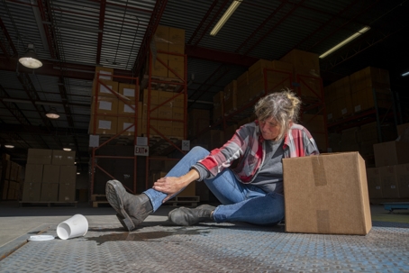 A warehouse, logistics safety topic. A female employee falls after slipping on a spilled drink. stock photo
