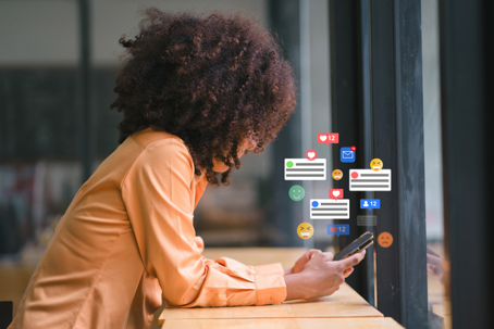 Smiling african american businesswoman engaging with social media on smartphone at modern workspace. stock photo