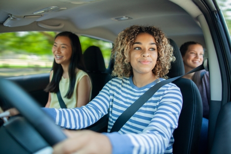 Young Multiracial teenager girl driving car while Asian friend sits in car with friends passenger stock photo