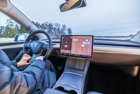 Close-up view of driver holding steering wheel inside Tesla Model 3 electric car with touchscreen displaying vehicle controls. stock photo