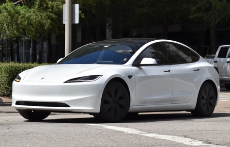 A portrait of a white Tesla Model 3 EV cruising in a downtown district stock photo