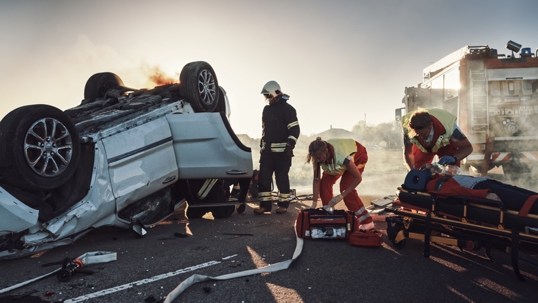 On the Car Crash Traffic Accident: Paramedics and Firefighters Rescue Injured Trapped Victims. Medics give First Aid to Female on Stretchers. Firemen Use Hydraulic Cutters Spreader to Open Vehicle stock photo